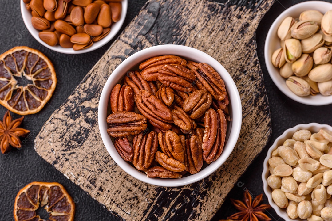 A imagem mostra uma variedade de nozes e frutas secas dispostas sobre uma tábua de madeira e um fundo escuro.