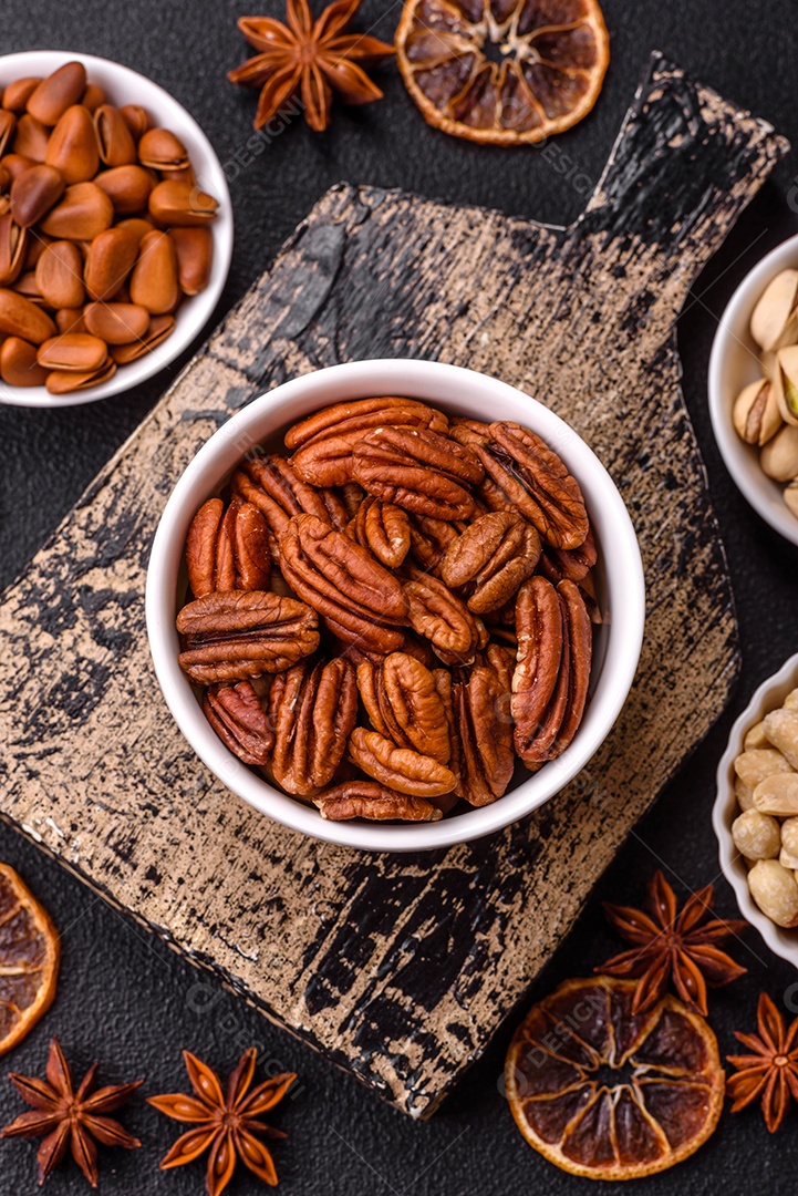 A imagem mostra uma variedade de nozes e frutas secas dispostas sobre uma tábua de madeira e um fundo escuro.