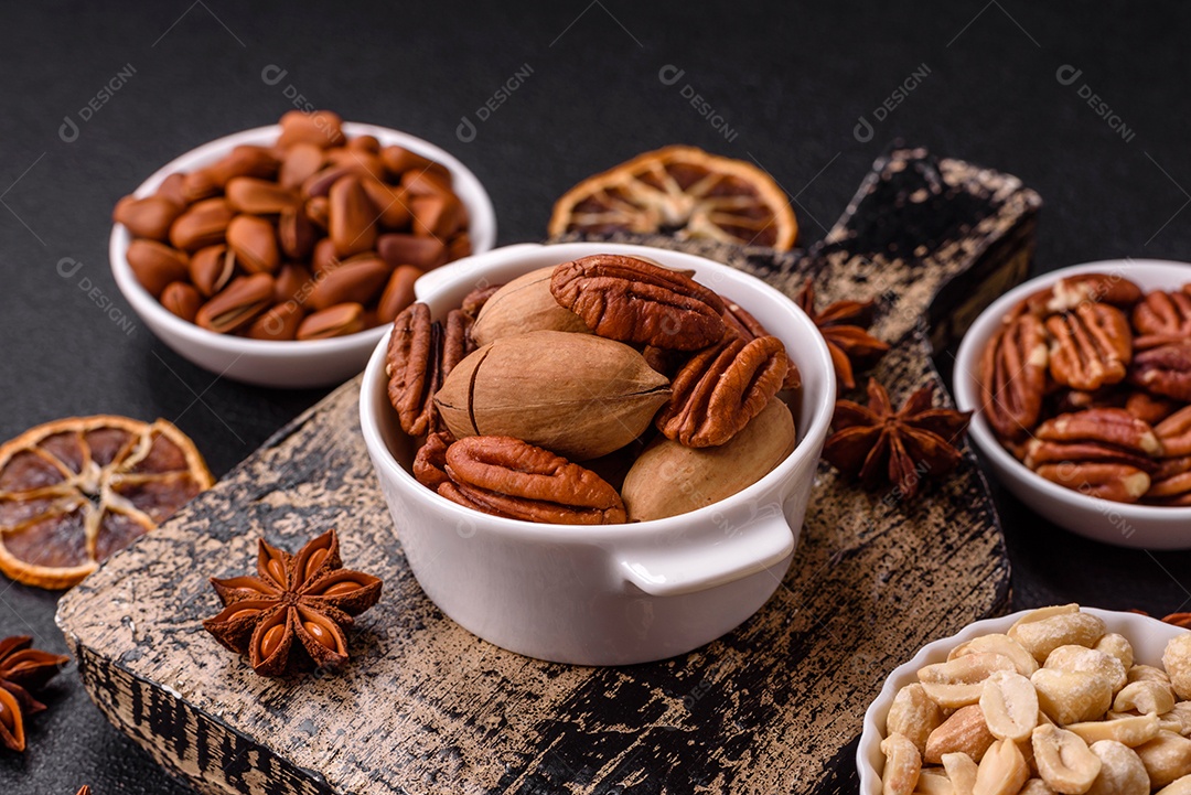 A imagem mostra uma variedade de nozes e frutas secas dispostas sobre uma tábua de madeira e um fundo escuro.