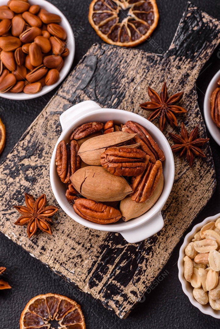 A imagem mostra uma variedade de nozes e frutas secas dispostas sobre uma tábua de madeira e um fundo escuro.