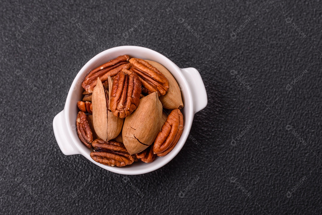 A imagem mostra uma variedade de nozes e frutas secas dispostas sobre uma tábua de madeira e um fundo escuro.