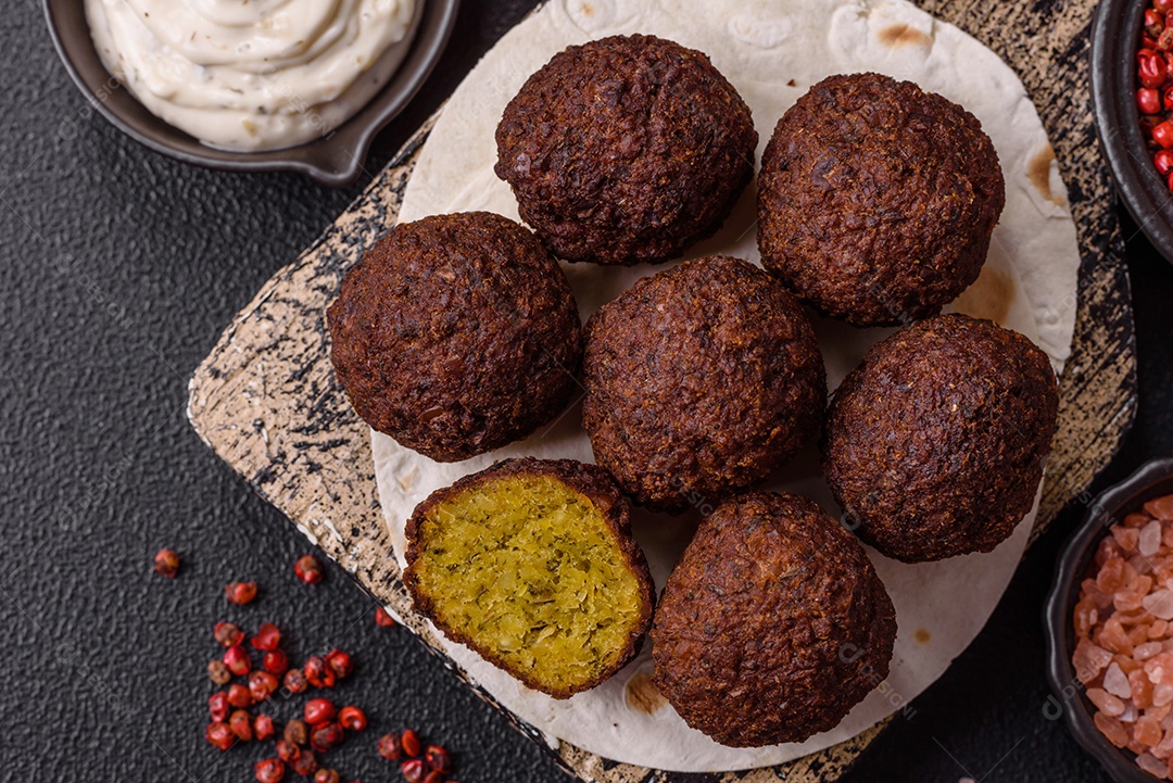 A imagem mostra bolinhos de faláfel servidos em um pão achatado.