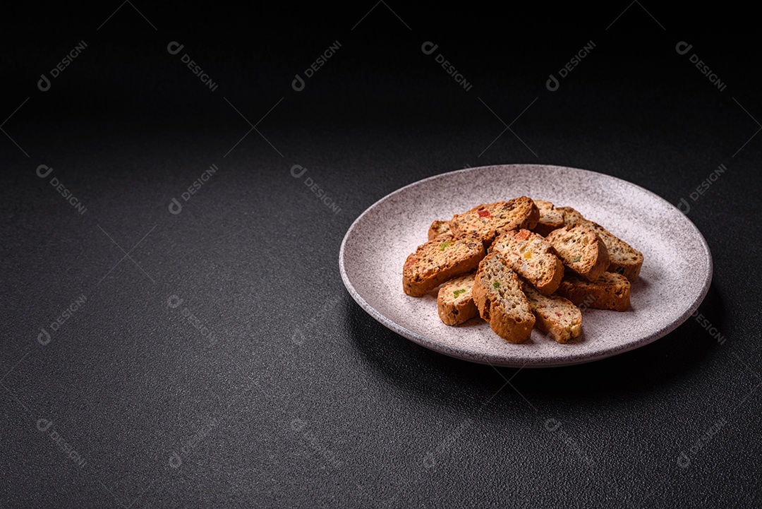 A imagem mostra uma seleção de biscoitos natalinos, incluindo biscoitos de pão de gengibre decorados e fatias de cantuccini com nozes e frutas cristalizadas.
