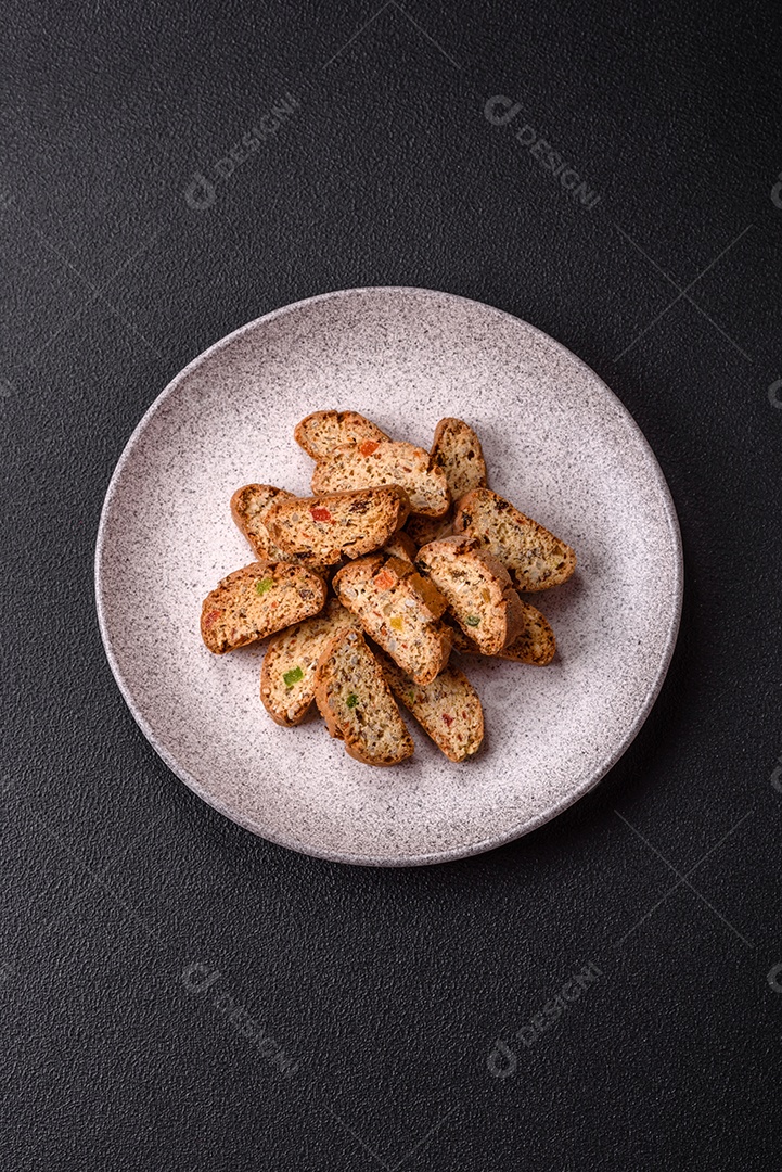 A imagem mostra uma seleção de biscoitos natalinos, incluindo biscoitos de pão de gengibre decorados e fatias de cantuccini com nozes e frutas cristalizadas.