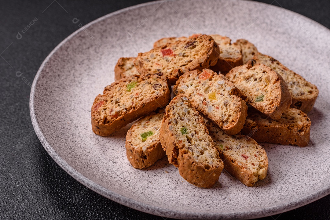 A imagem mostra uma seleção de biscoitos natalinos, incluindo biscoitos de pão de gengibre decorados e fatias de cantuccini com nozes e frutas cristalizadas.