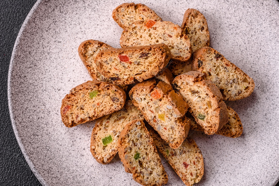 A imagem mostra uma seleção de biscoitos natalinos, incluindo biscoitos de pão de gengibre decorados e fatias de cantuccini com nozes e frutas cristalizadas.