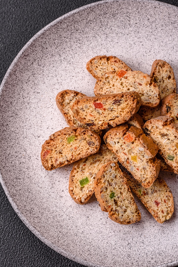 A imagem mostra uma seleção de biscoitos natalinos, incluindo biscoitos de pão de gengibre decorados e fatias de cantuccini com nozes e frutas cristalizadas.