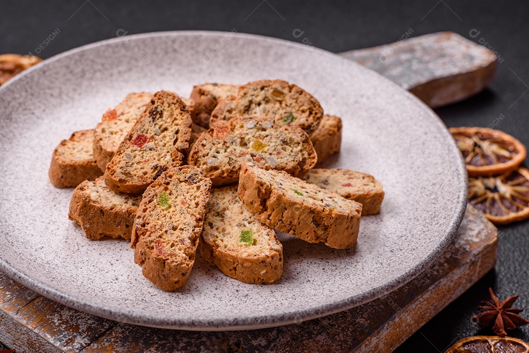 A imagem mostra uma seleção de biscoitos natalinos, incluindo biscoitos de pão de gengibre decorados e fatias de cantuccini com nozes e frutas cristalizadas.