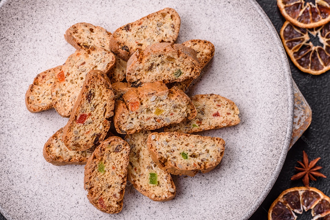A imagem mostra uma seleção de biscoitos natalinos, incluindo biscoitos de pão de gengibre decorados e fatias de cantuccini com nozes e frutas cristalizadas.