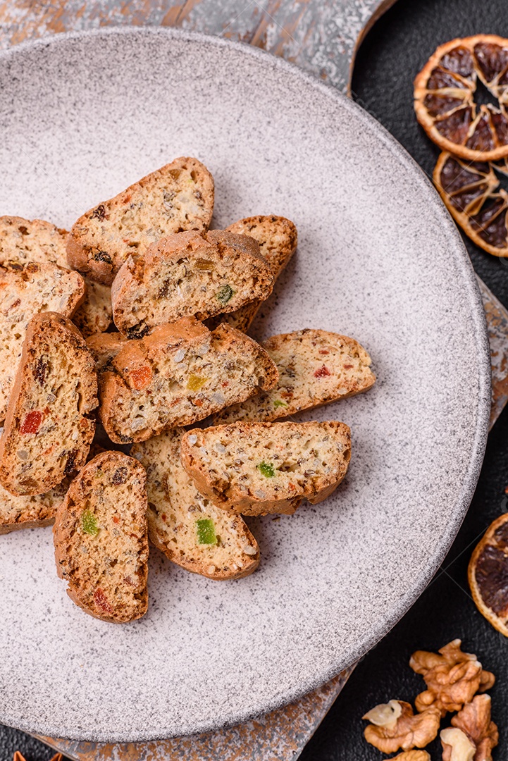 A imagem mostra uma seleção de biscoitos natalinos, incluindo biscoitos de pão de gengibre decorados e fatias de cantuccini com nozes e frutas cristalizadas.