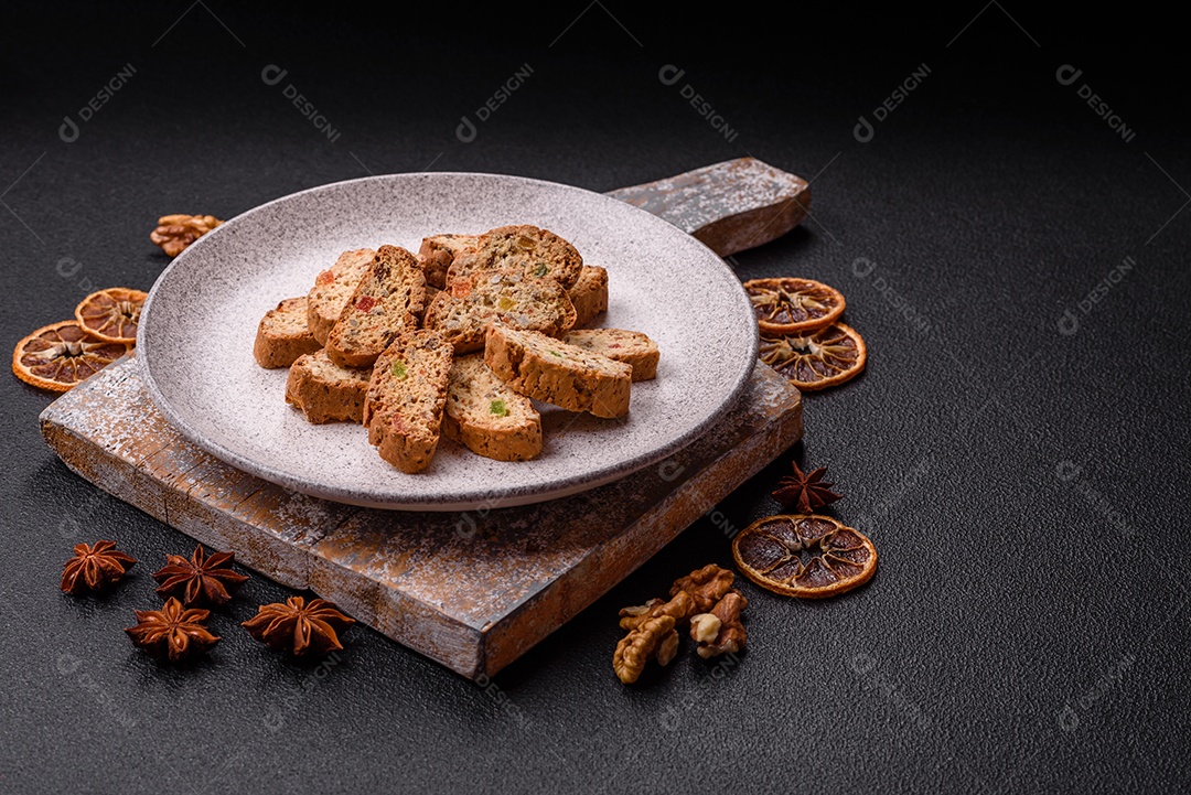 A imagem mostra uma seleção de biscoitos natalinos, incluindo biscoitos de pão de gengibre decorados e fatias de cantuccini com nozes e frutas cristalizadas.