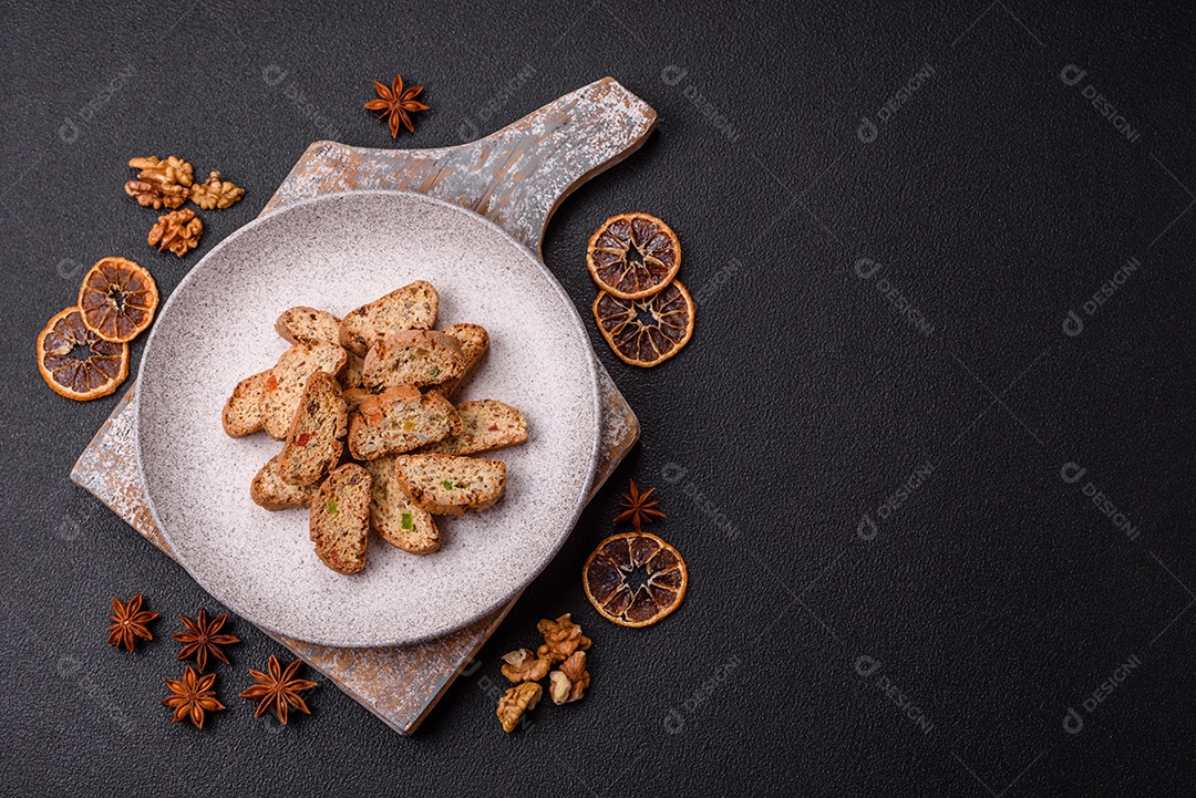 A imagem mostra uma seleção de biscoitos natalinos, incluindo biscoitos de pão de gengibre decorados e fatias de cantuccini com nozes e frutas cristalizadas.