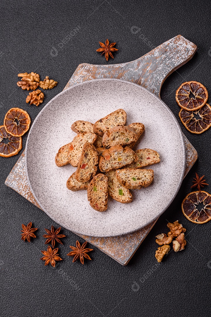 A imagem mostra uma seleção de biscoitos natalinos, incluindo biscoitos de pão de gengibre decorados e fatias de cantuccini com nozes e frutas cristalizadas.