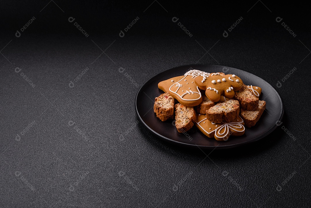 A imagem mostra uma seleção de biscoitos natalinos, incluindo biscoitos de pão de gengibre decorados e fatias de cantuccini com nozes e frutas cristalizadas.