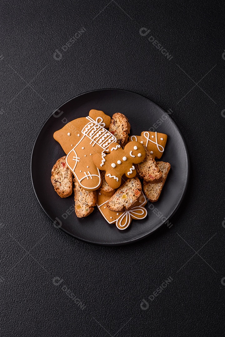 A imagem mostra uma seleção de biscoitos natalinos, incluindo biscoitos de pão de gengibre decorados e fatias de cantuccini com nozes e frutas cristalizadas.