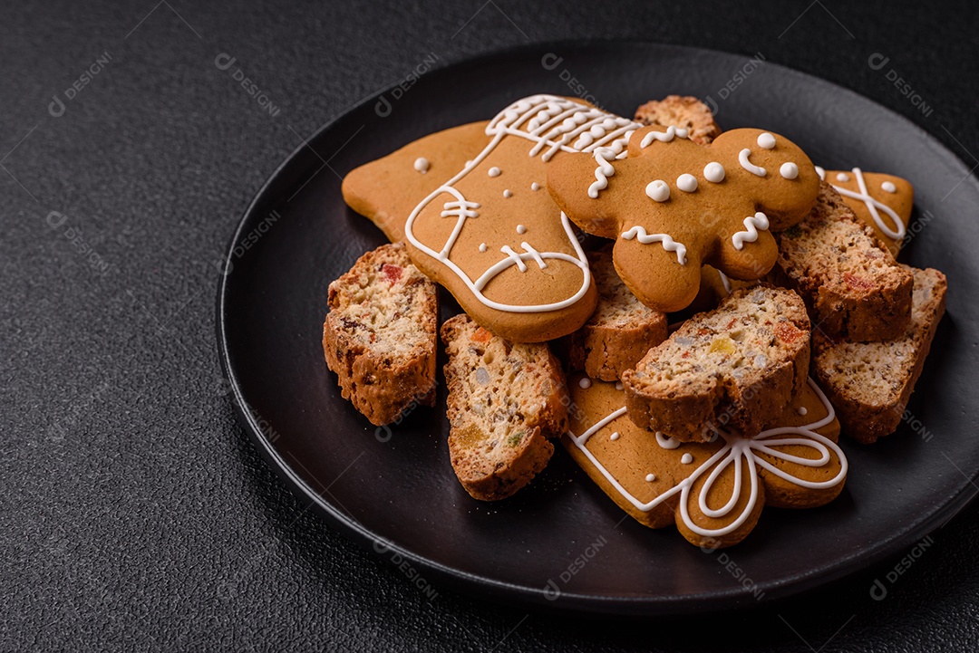 A imagem mostra uma seleção de biscoitos natalinos, incluindo biscoitos de pão de gengibre decorados e fatias de cantuccini com nozes e frutas cristalizadas.