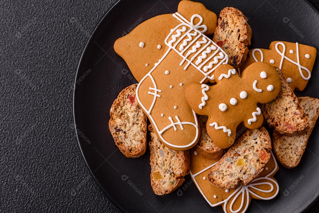A imagem mostra uma seleção de biscoitos natalinos, incluindo biscoitos de pão de gengibre decorados e fatias de cantuccini com nozes e frutas cristalizadas.