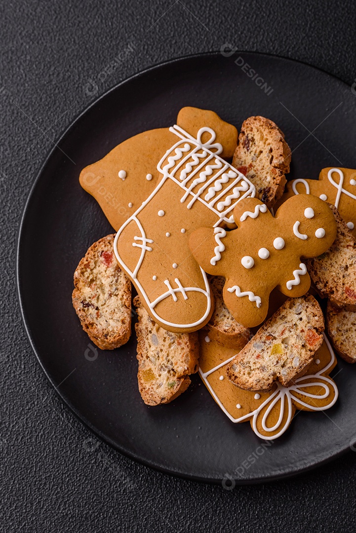 A imagem mostra uma seleção de biscoitos natalinos, incluindo biscoitos de pão de gengibre decorados e fatias de cantuccini com nozes e frutas cristalizadas.