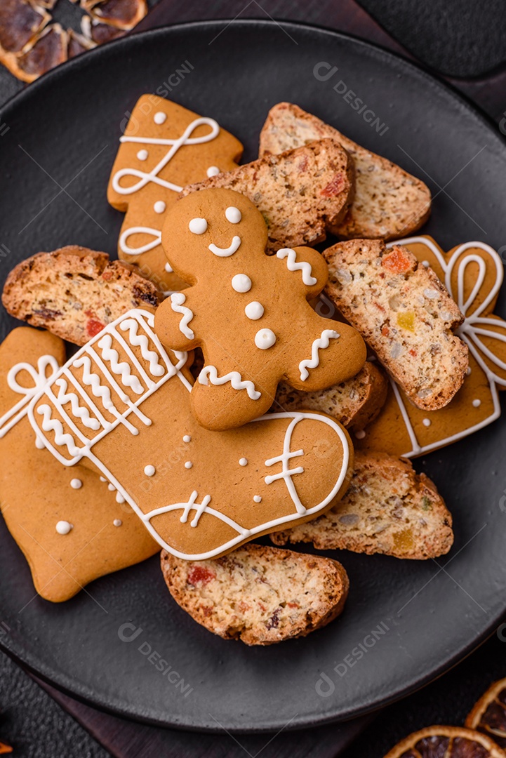 A imagem mostra uma seleção de biscoitos natalinos, incluindo biscoitos de pão de gengibre decorados e fatias de cantuccini com nozes e frutas cristalizadas.