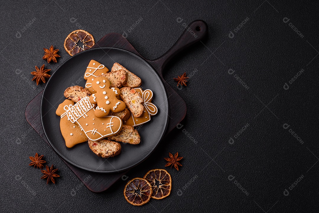 A imagem mostra uma seleção de biscoitos natalinos, incluindo biscoitos de pão de gengibre decorados e fatias de cantuccini com nozes e frutas cristalizadas.