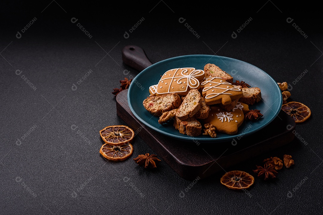 A imagem mostra uma seleção de biscoitos natalinos, incluindo biscoitos de pão de gengibre decorados e fatias de cantuccini com nozes e frutas cristalizadas.