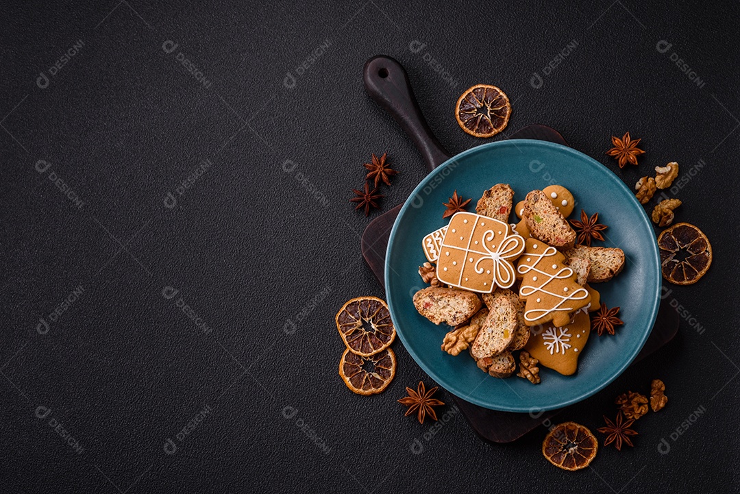 A imagem mostra uma seleção de biscoitos natalinos, incluindo biscoitos de pão de gengibre decorados e fatias de cantuccini com nozes e frutas cristalizadas.