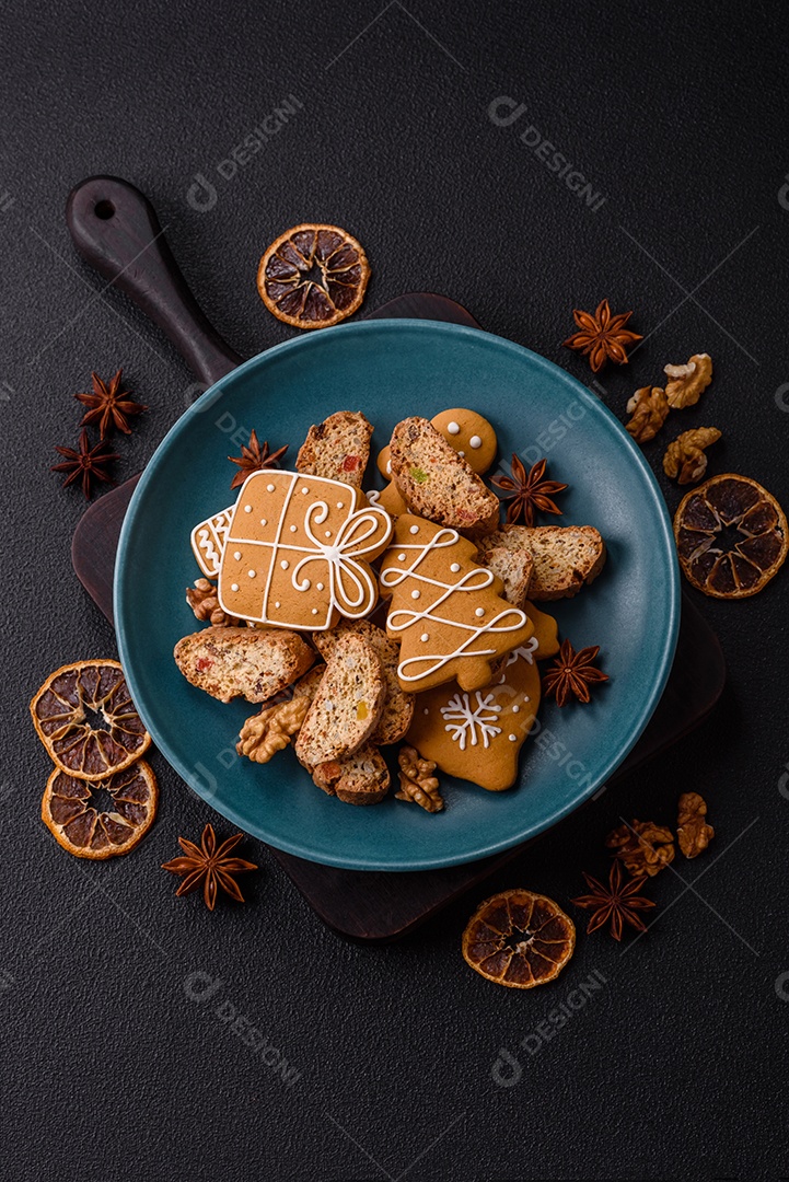 A imagem mostra uma seleção de biscoitos natalinos, incluindo biscoitos de pão de gengibre decorados e fatias de cantuccini com nozes e frutas cristalizadas.