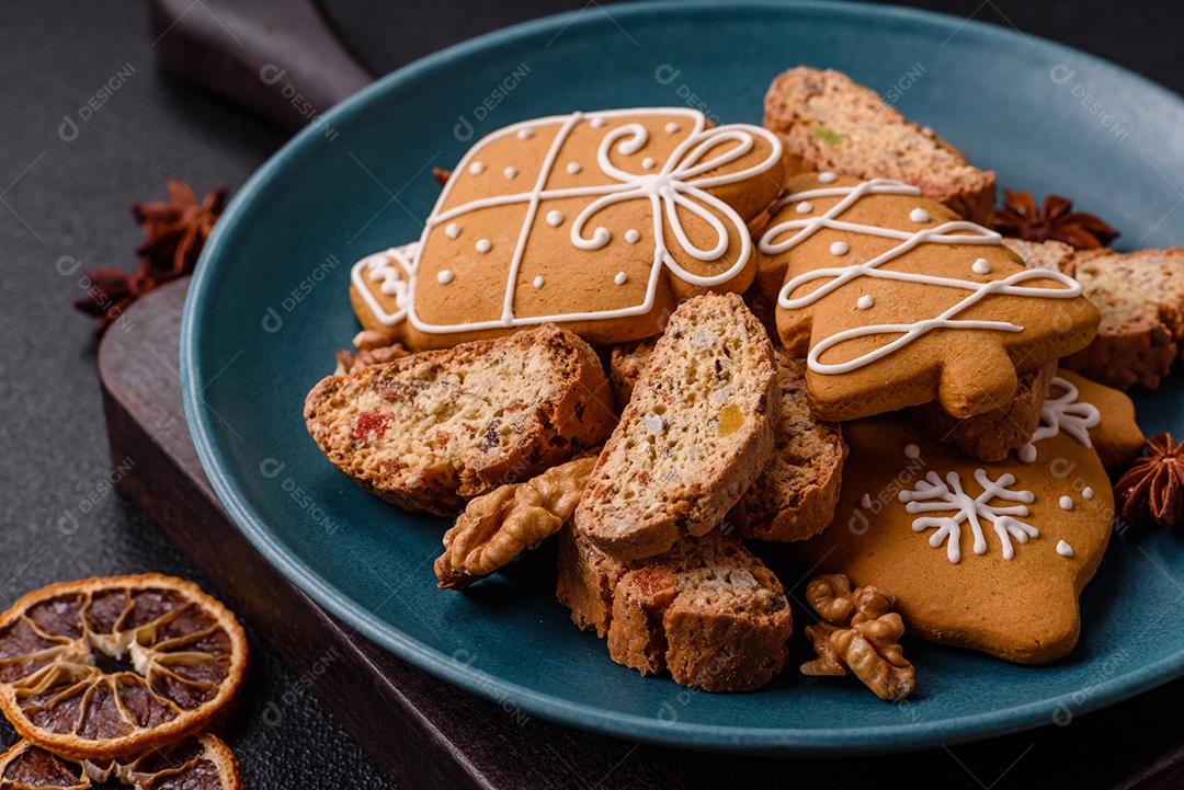 A imagem mostra uma seleção de biscoitos natalinos, incluindo biscoitos de pão de gengibre decorados e fatias de cantuccini com nozes e frutas cristalizadas.