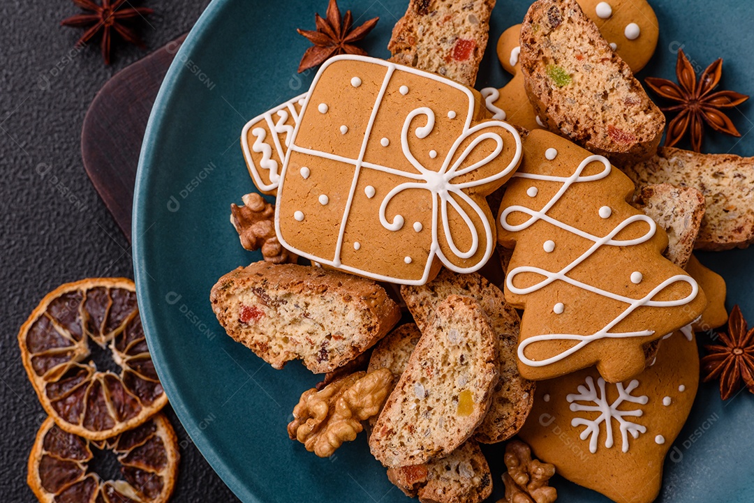 A imagem mostra uma seleção de biscoitos natalinos, incluindo biscoitos de pão de gengibre decorados e fatias de cantuccini com nozes e frutas cristalizadas.