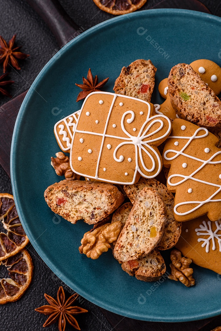 A imagem mostra uma seleção de biscoitos natalinos, incluindo biscoitos de pão de gengibre decorados e fatias de cantuccini com nozes e frutas cristalizadas.