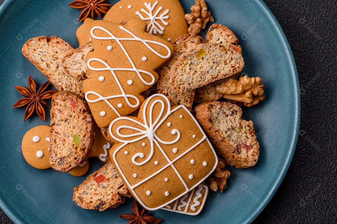 A imagem mostra uma seleção de biscoitos natalinos, incluindo biscoitos de pão de gengibre decorados e fatias de cantuccini com nozes e frutas cristalizadas.