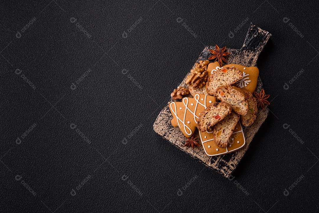 A imagem mostra uma seleção de biscoitos natalinos, incluindo biscoitos de pão de gengibre decorados e fatias de cantuccini com nozes e frutas cristalizadas.
