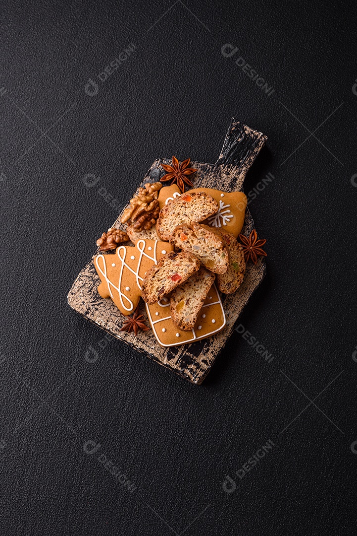 A imagem mostra uma seleção de biscoitos natalinos, incluindo biscoitos de pão de gengibre decorados e fatias de cantuccini com nozes e frutas cristalizadas.