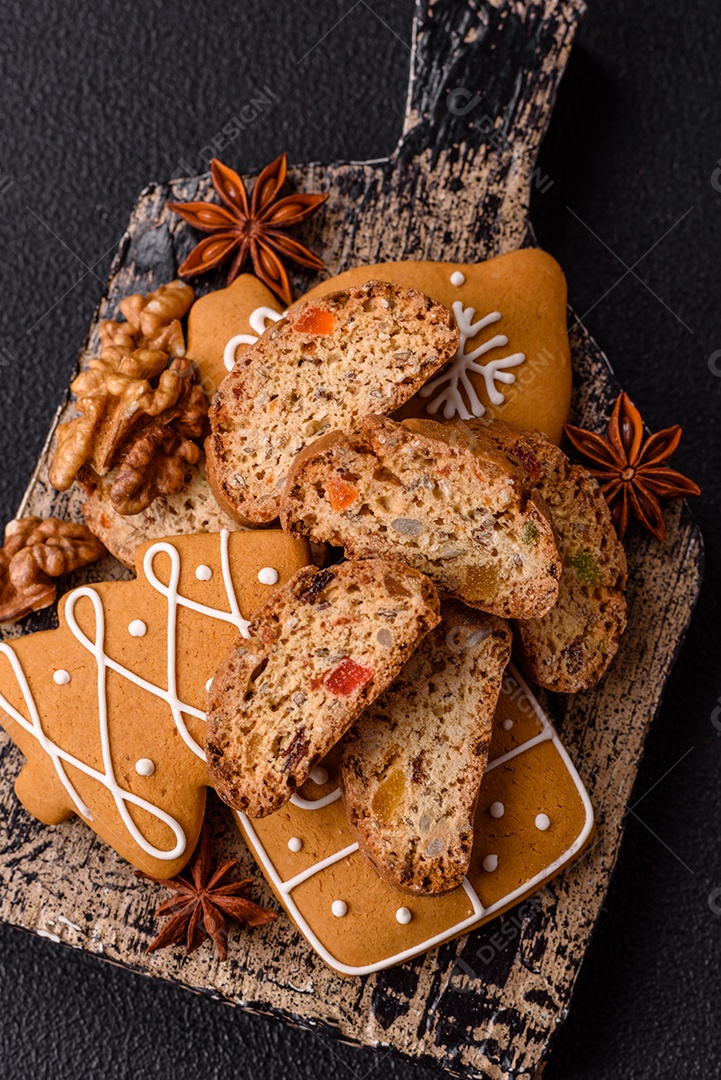 A imagem mostra uma seleção de biscoitos natalinos, incluindo biscoitos de pão de gengibre decorados e fatias de cantuccini com nozes e frutas cristalizadas.