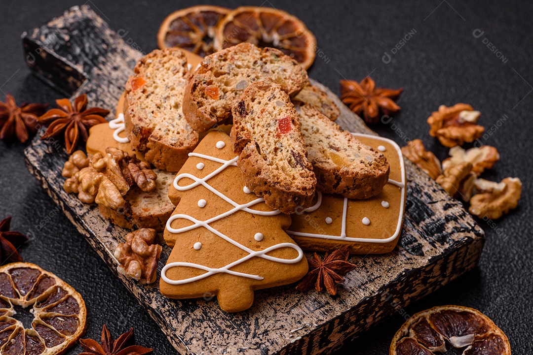 A imagem mostra uma seleção de biscoitos natalinos, incluindo biscoitos de pão de gengibre decorados e fatias de cantuccini com nozes e frutas cristalizadas.