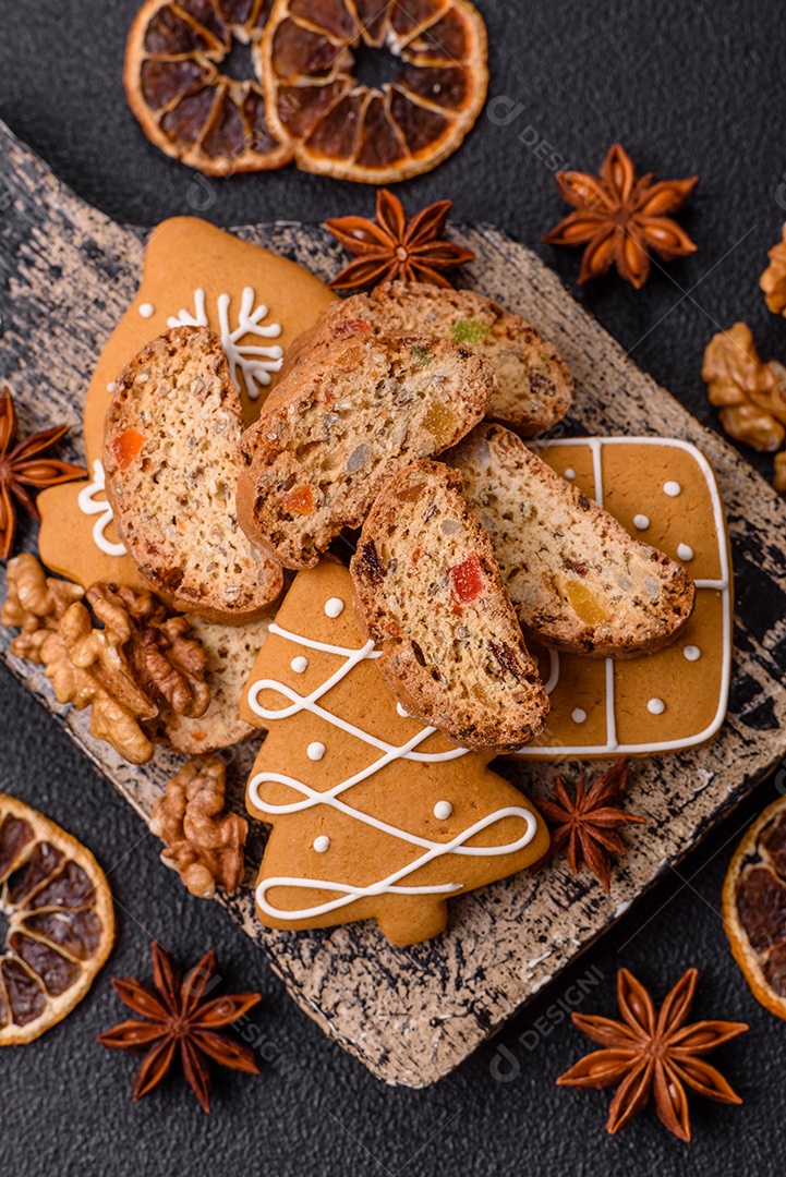 A imagem mostra uma seleção de biscoitos natalinos, incluindo biscoitos de pão de gengibre decorados e fatias de cantuccini com nozes e frutas cristalizadas.