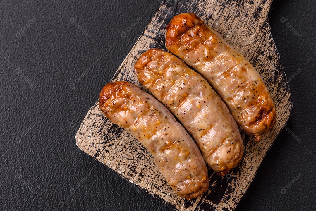 Três linguiças ou salsichas grelhadas são apresentadas em um prato, com temperos e tomates-cereja cortados.