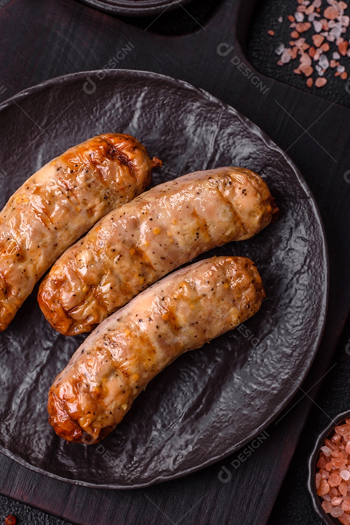 Três linguiças ou salsichas grelhadas são apresentadas em um prato, com temperos e tomates-cereja cortados.