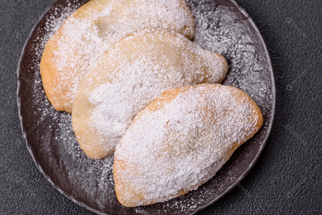 A imagem mostra biscoitos ou pastéis polvilhados com açúcar de confeiteiro, que podem ser semelhantes ao pastel de carne com açúcar