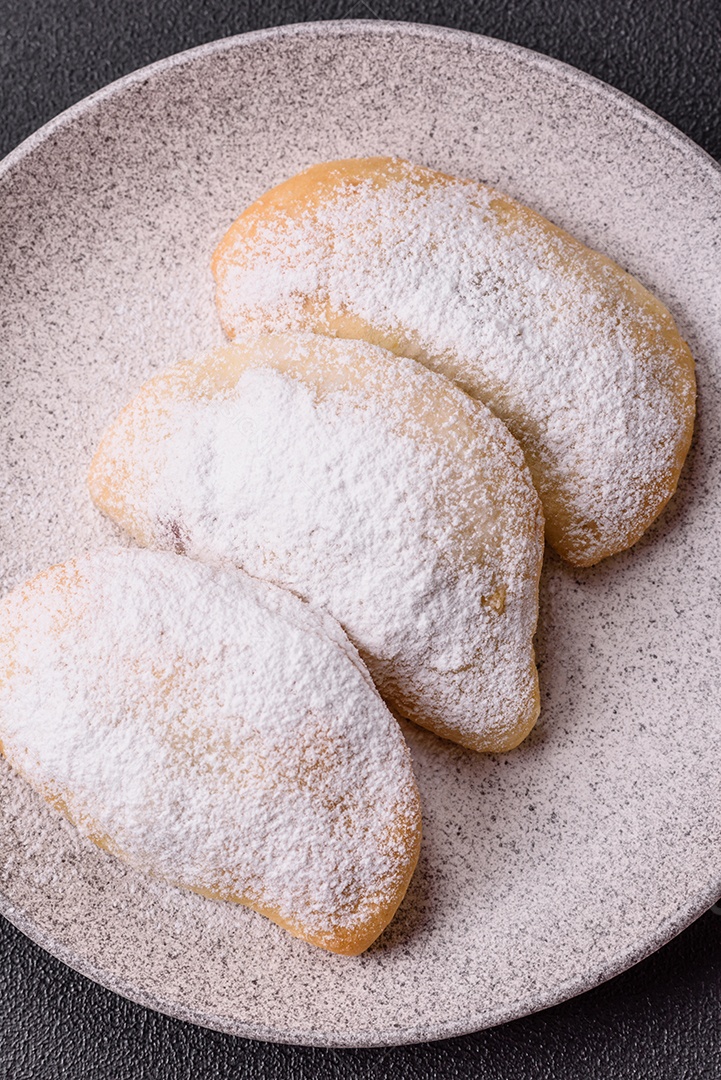 A imagem mostra biscoitos ou pastéis polvilhados com açúcar de confeiteiro, que podem ser semelhantes ao pastel de carne com açúcar