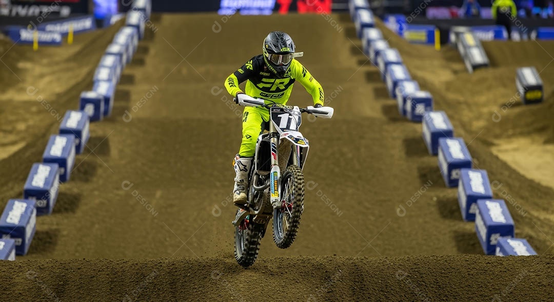 Motociclista praticando motocross sob uma pista com obstáculos.